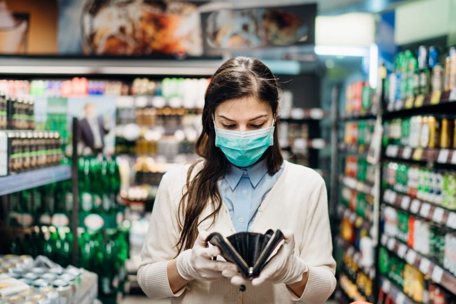 Worried woman with mask groceries shopping in supermarket looking at empty wallet
