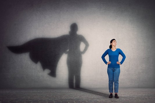 Woman leader standing triumphantly with caped shadow