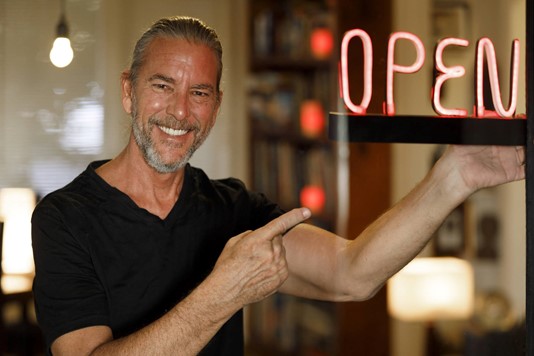 Small business owner points to neon “OPEN” sign
